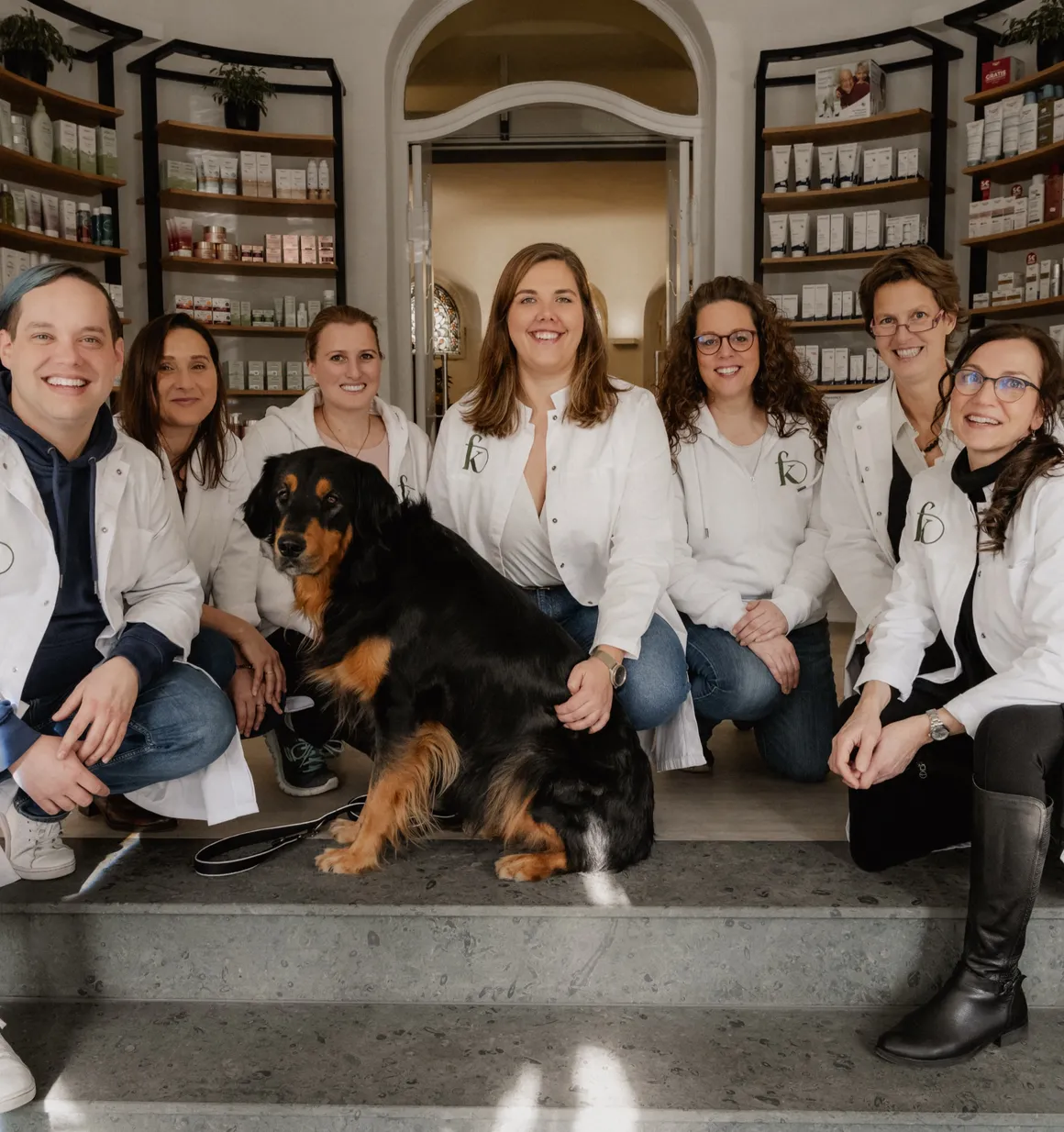 Das Team der Fritz-König-Apotheke sitzt mit einem Hund auf den Stufen am Eingang der Offizin