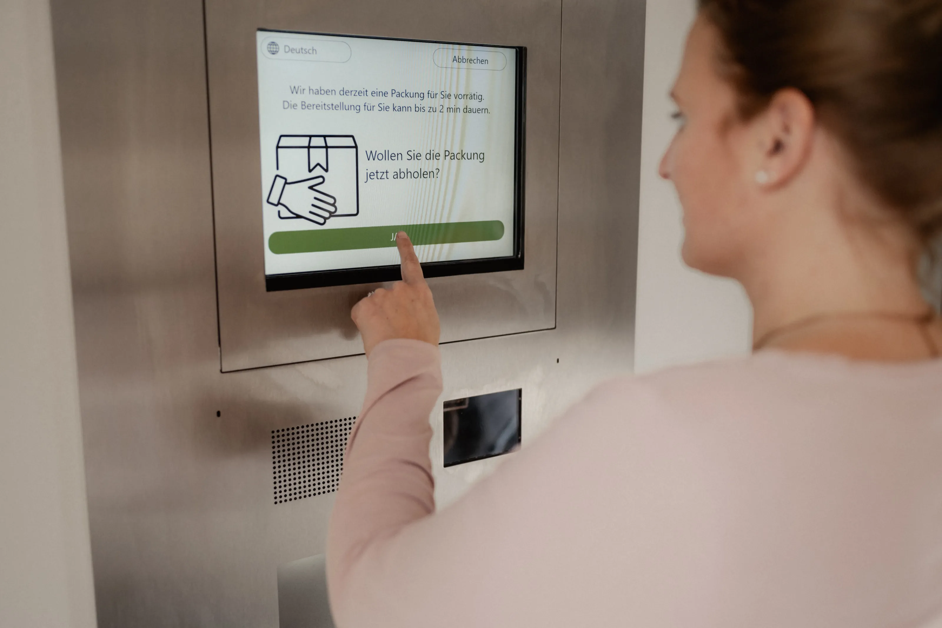 Eine Person tippt am 24-Stunden-Abholautomaten auf den Bildschirm: Wollen Sie die Packung jetzt abholen?