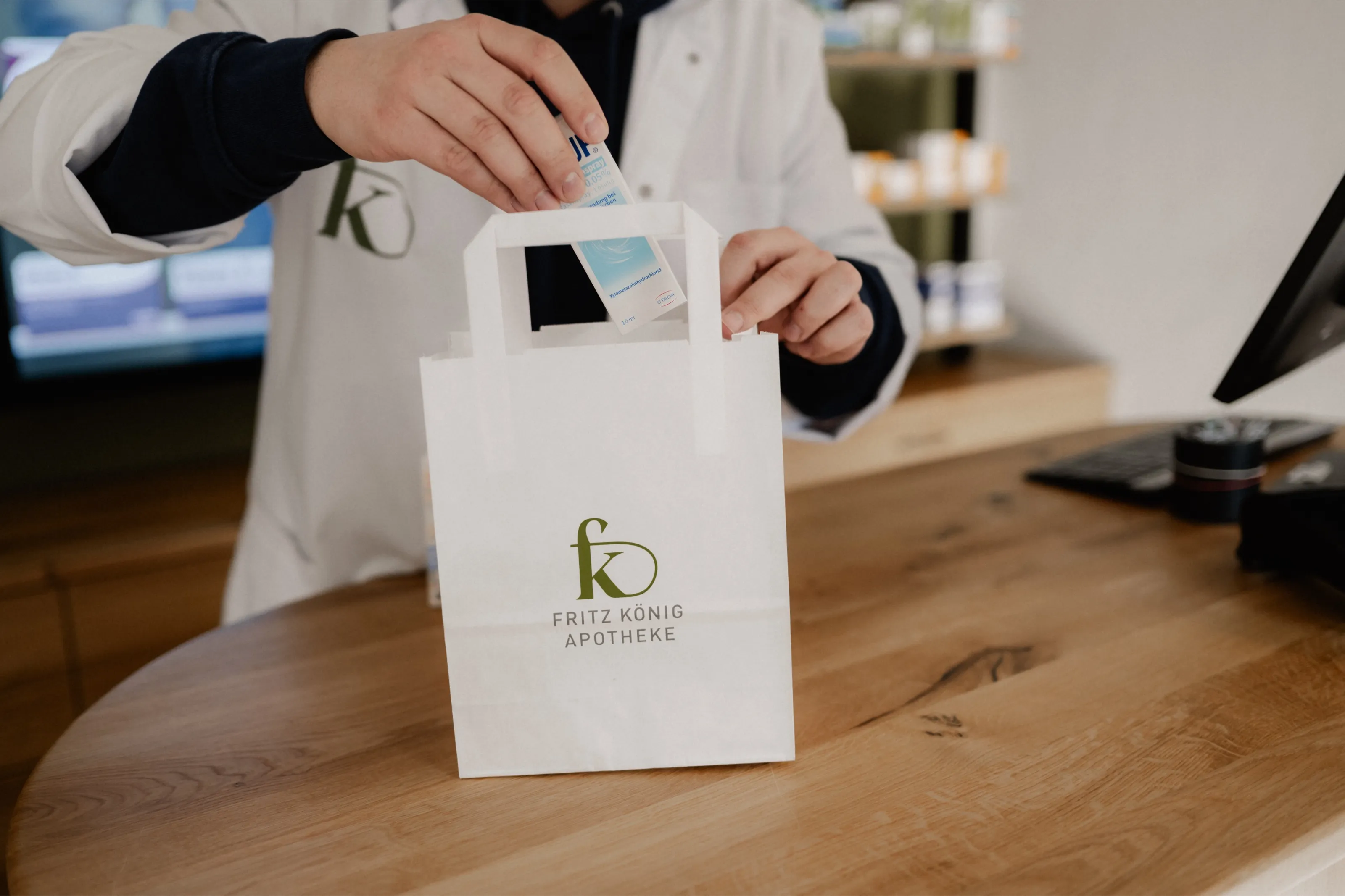 Eine Papiertüte mit dem Logo der Fritz-König-Apotheke wird am Tresen mit einem Medikament befüllt