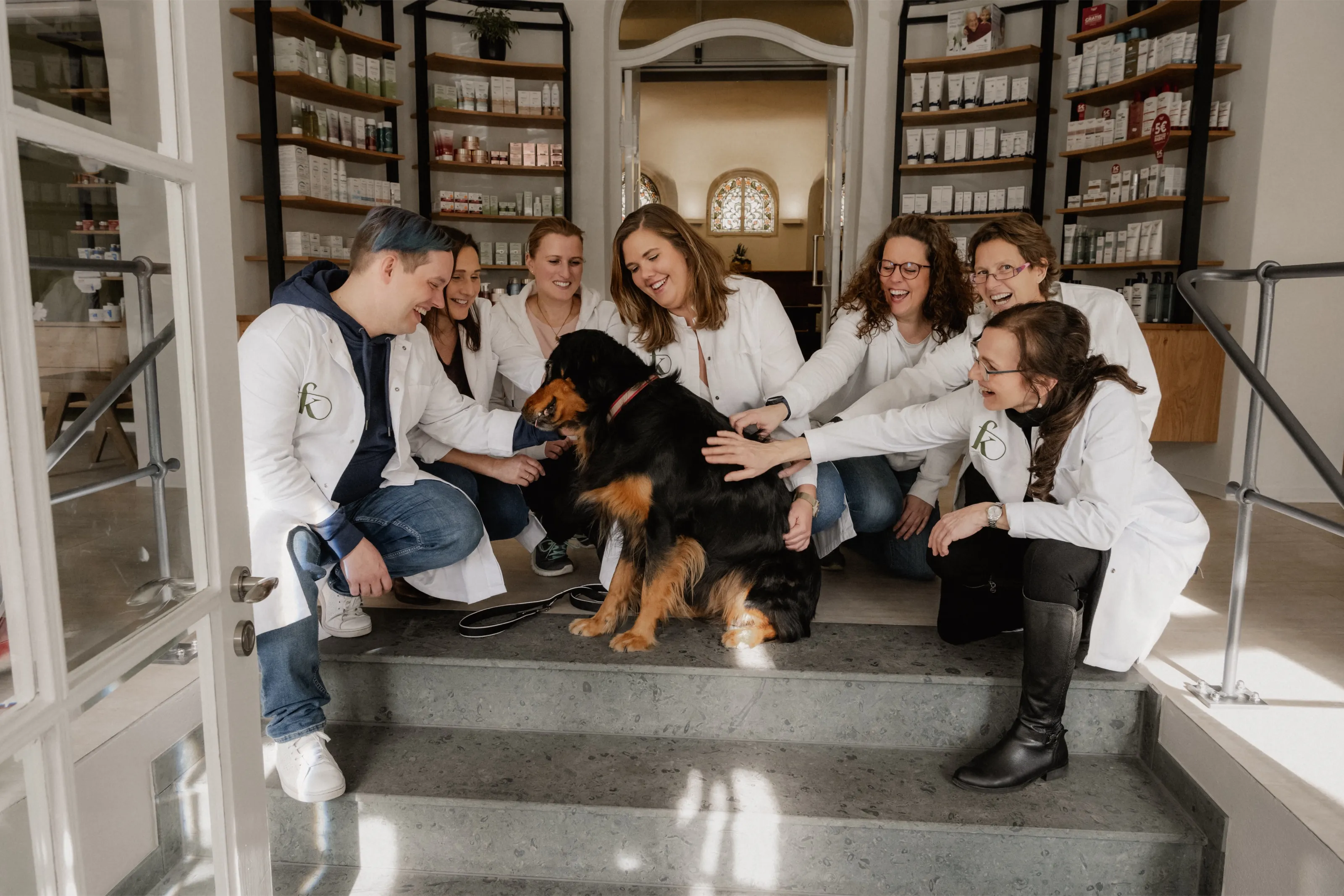 Das Team der Fritz-König-Apotheke steht lachend um einen Hund auf den Stufen