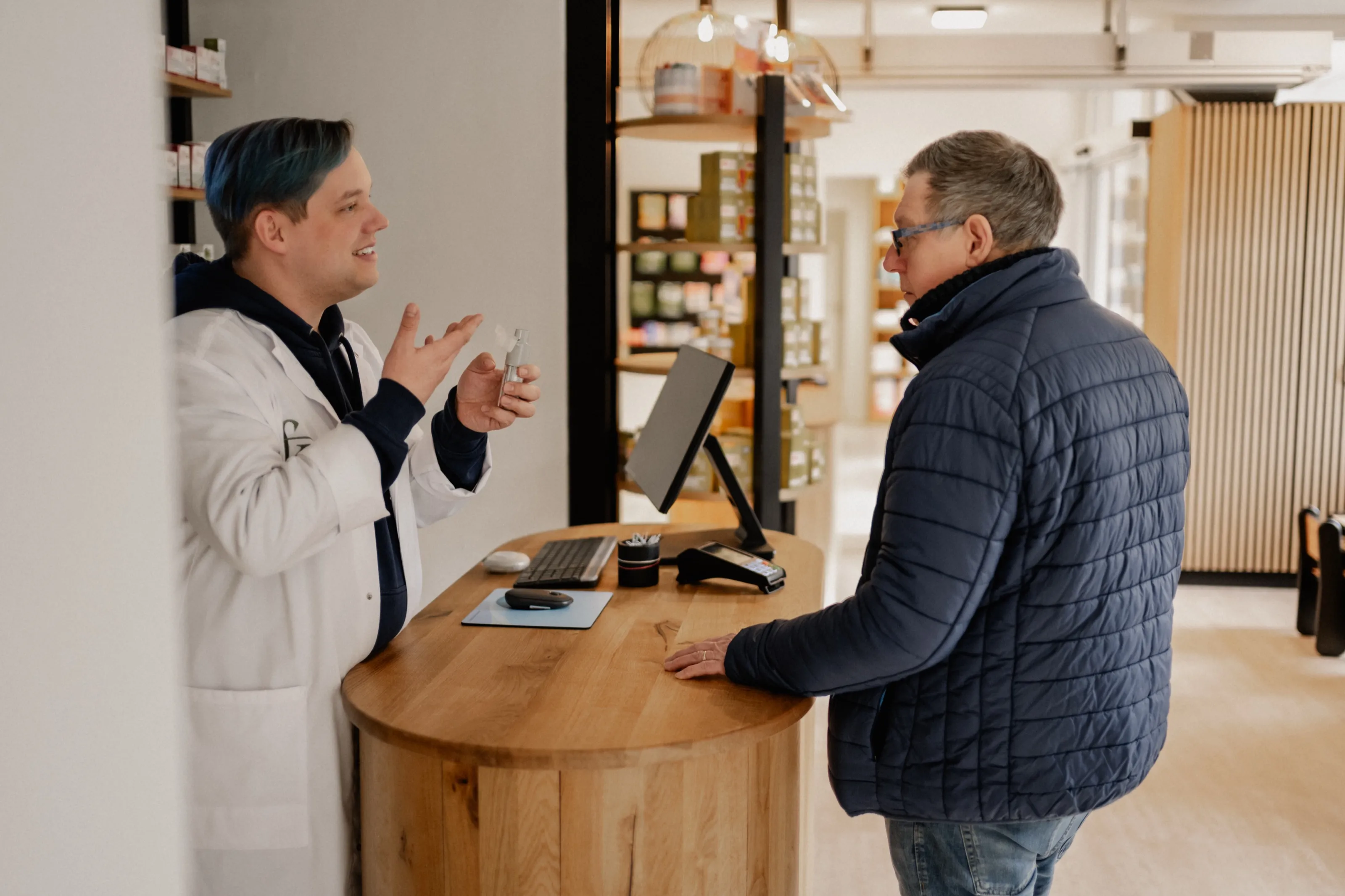 Ein Apotheker erklärt einem Kunden am Tresen die Handhabung eines Inhalators